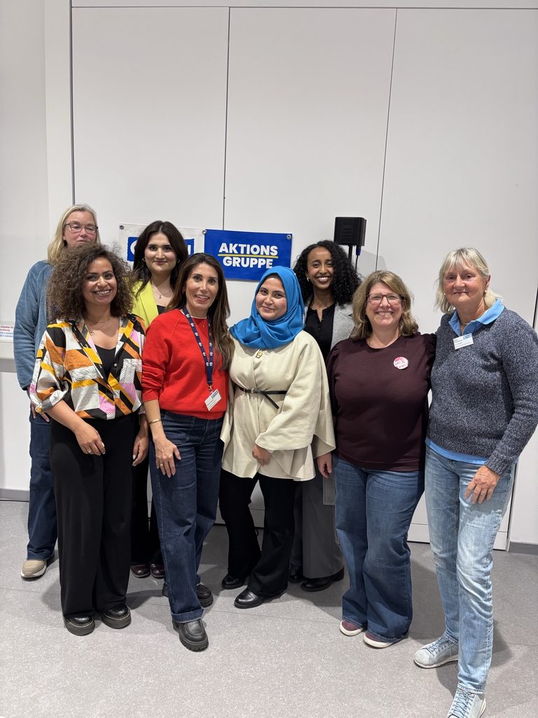 Eine Gruppe von acht Frauen, die gemeinsam vor einem Schild der Aktionsgruppe posieren.